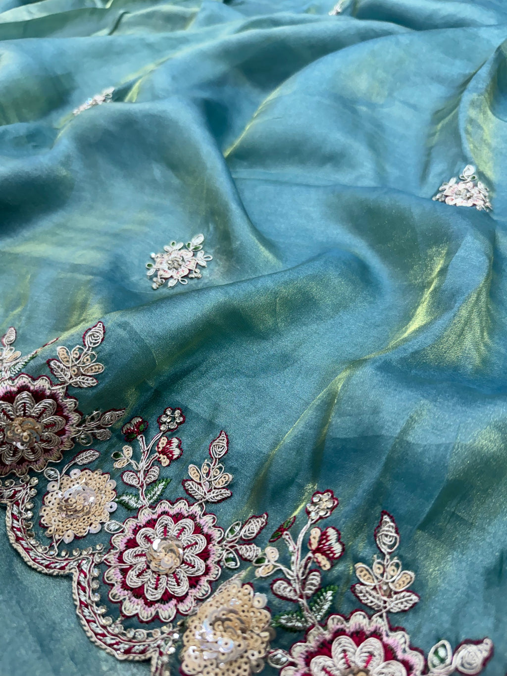 Teal fabric with intricate floral embroidery and embellishments