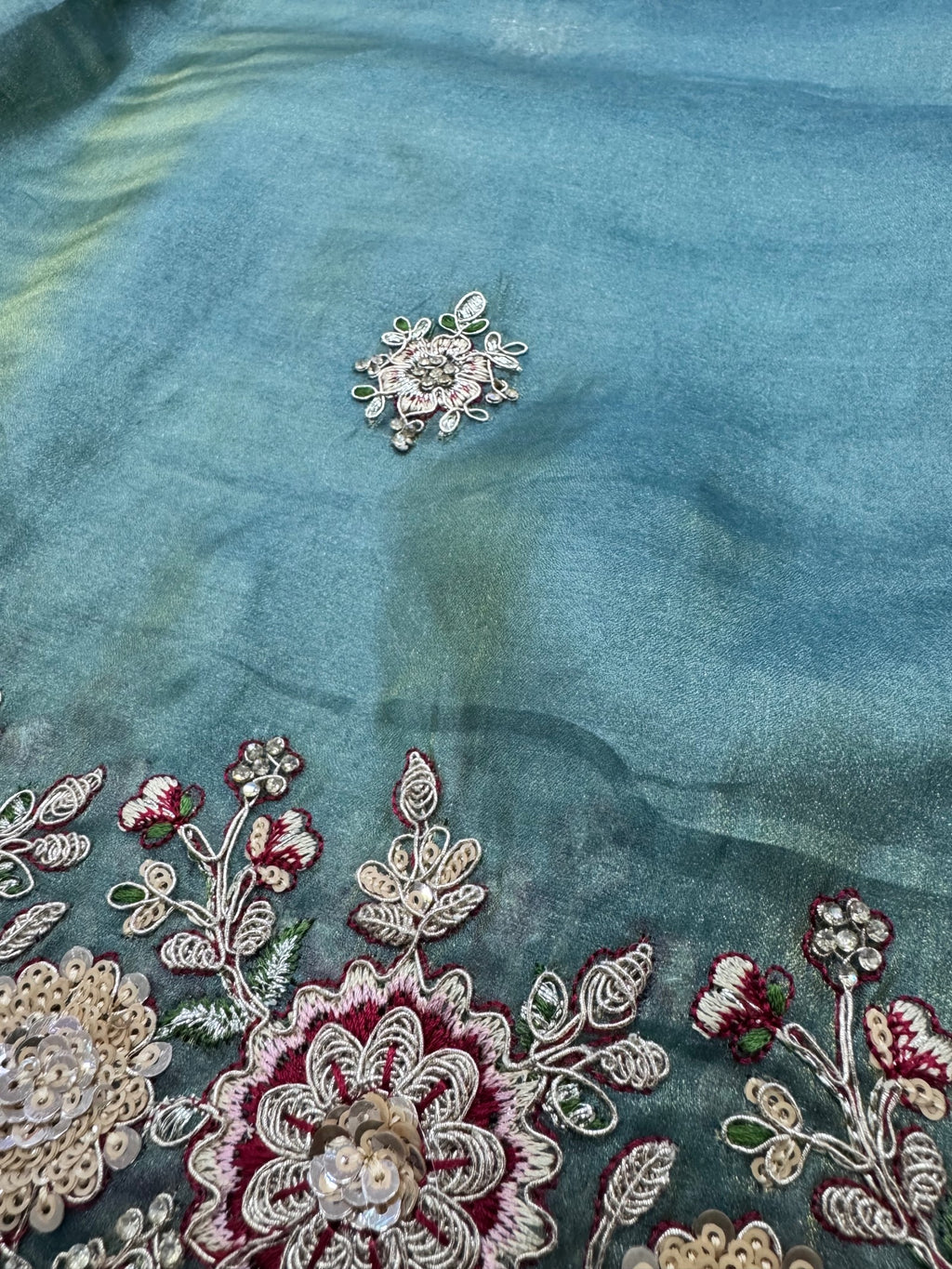 Close-up of embroidered fabric with floral patterns and beads on a teal background