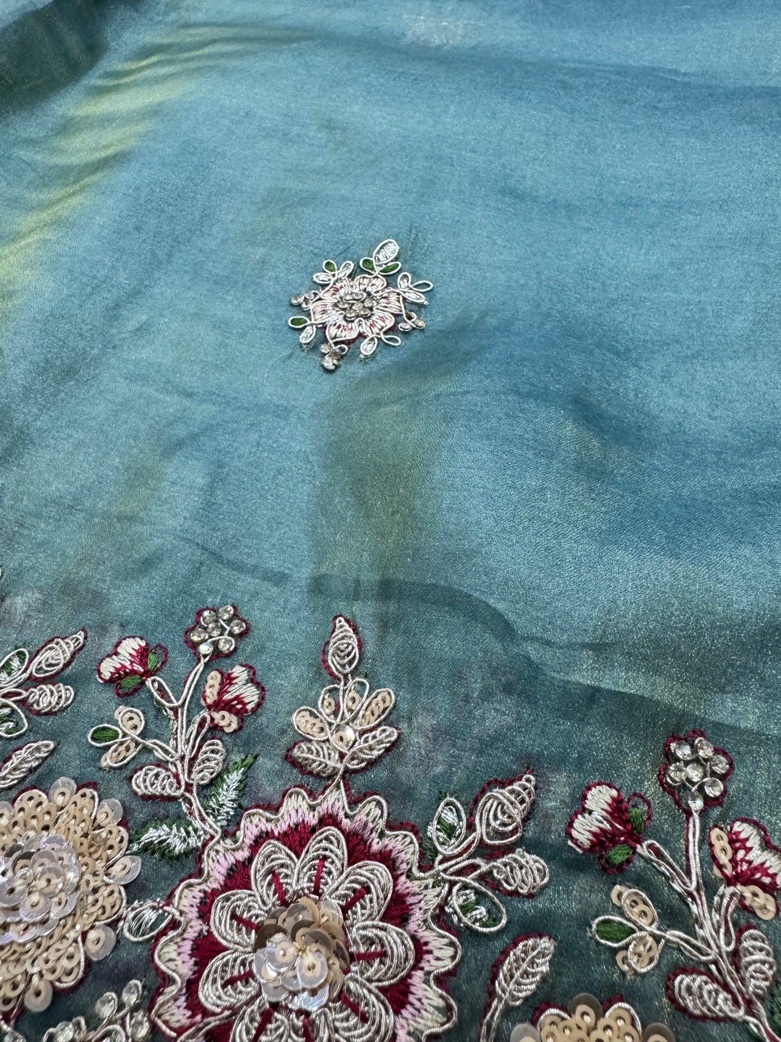 Close-up of embroidered fabric with floral patterns and beads on a teal background
