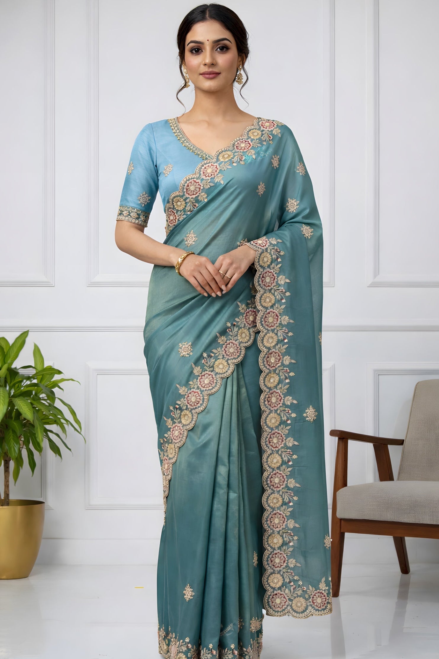 Woman wearing a teal saree with gold embroidery in a minimalistic room.
