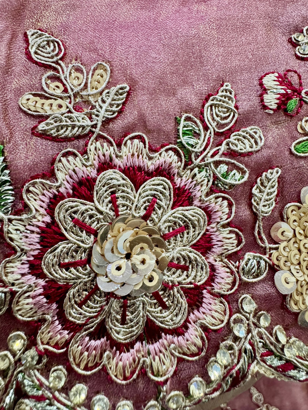 Close-up of intricate floral embroidery with sequins on a pink fabric background