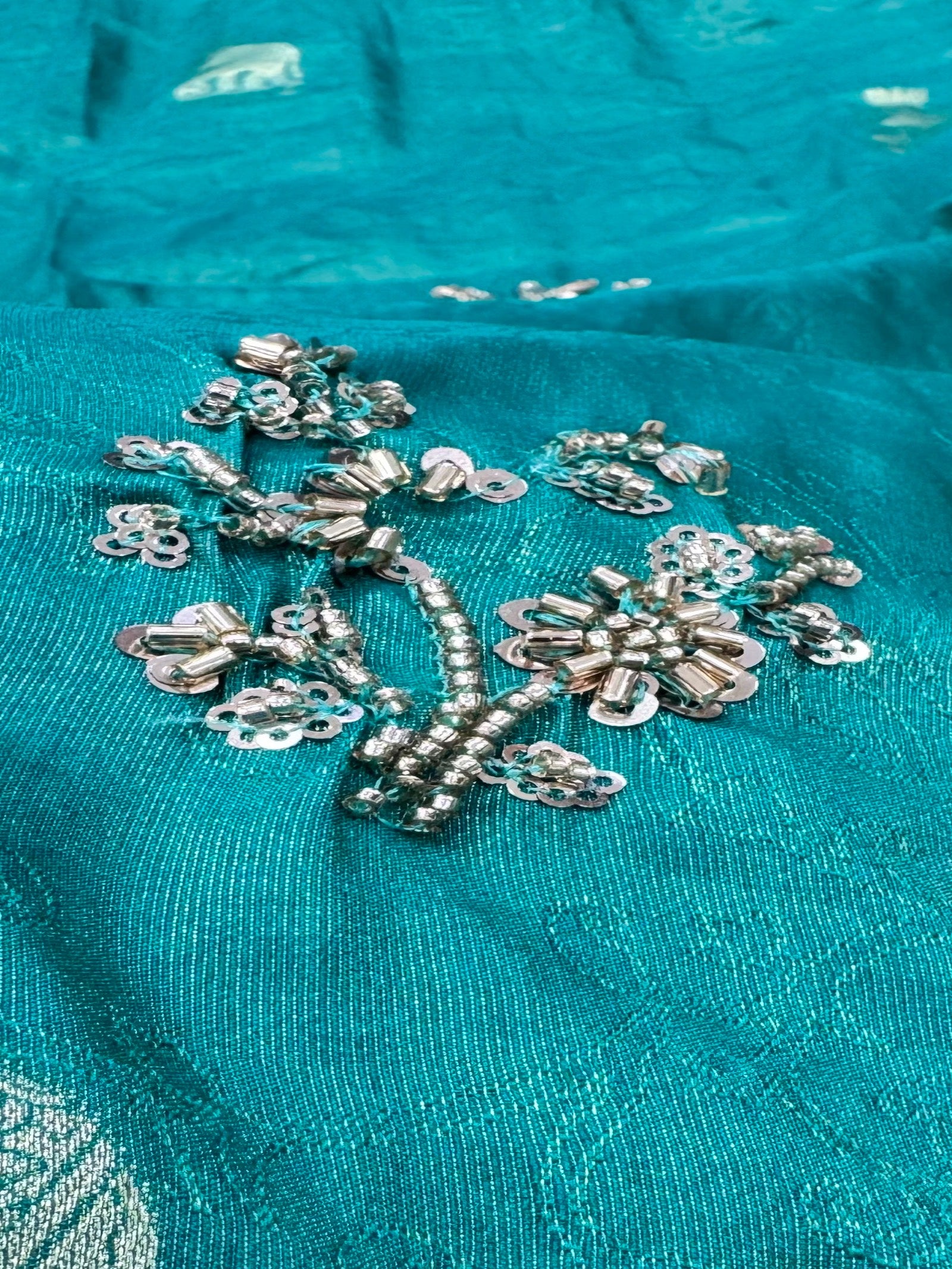Close-up of silver floral embroidery on teal fabric