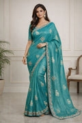 Woman wearing a teal saree with white patterns in an indoor setting
