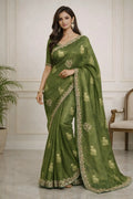 Woman wearing a green saree with gold embroidery in an indoor setting.