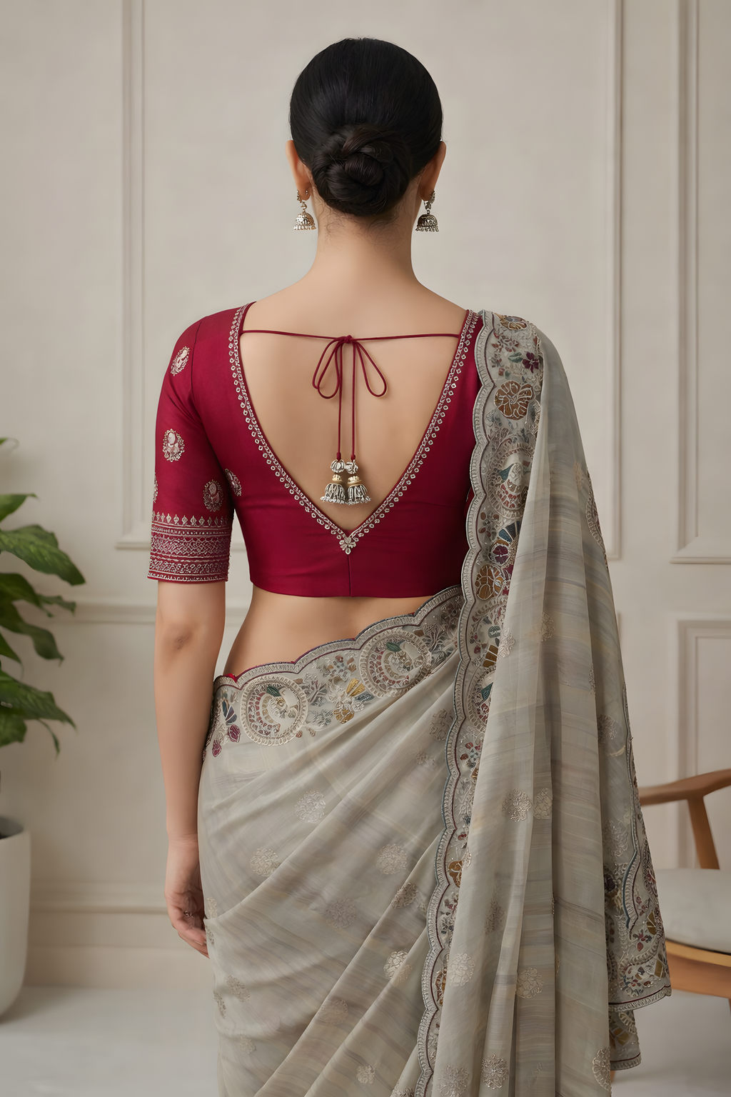 Woman wearing a red blouse and beige saree with intricate patterns indoors.