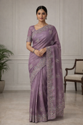 Woman wearing a purple saree with silver embroidery in an indoor setting.