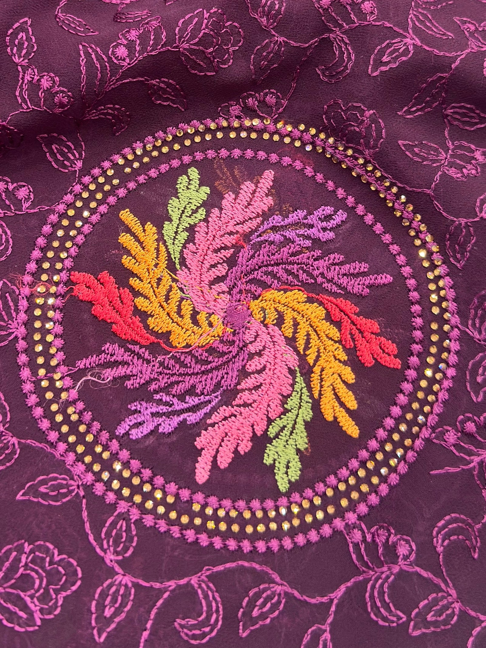 Close-up of embroidered fabric with colorful floral design on a purple background