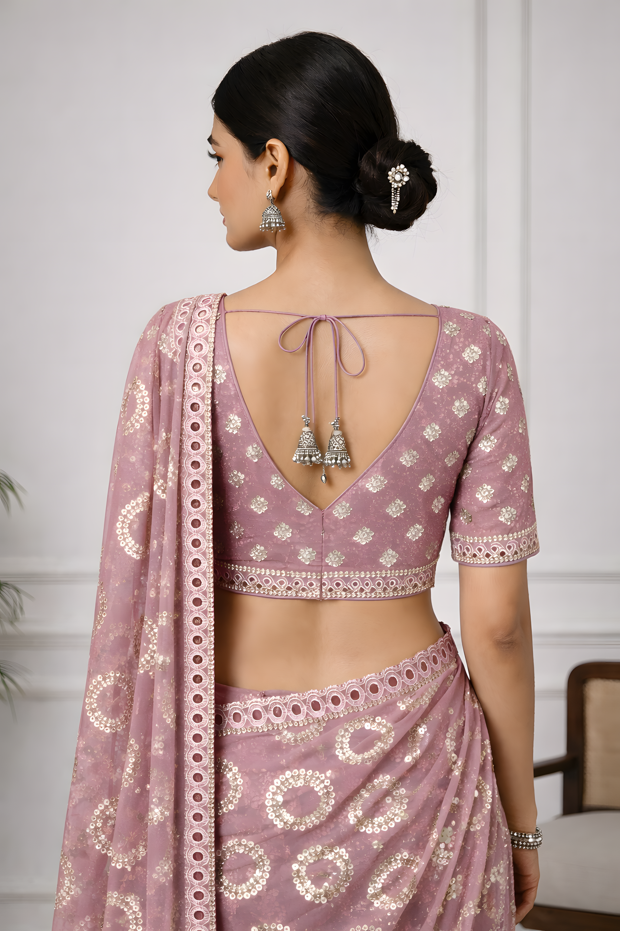 Woman wearing a pink saree with intricate patterns and jewelry against a white background