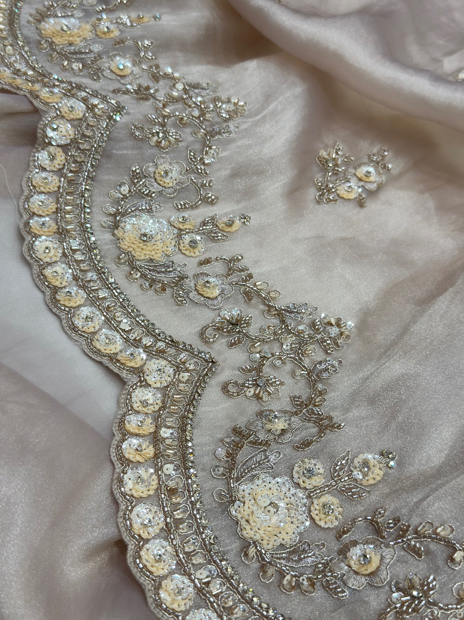 Close-up of intricately embroidered fabric with gold and silver details on a beige background.