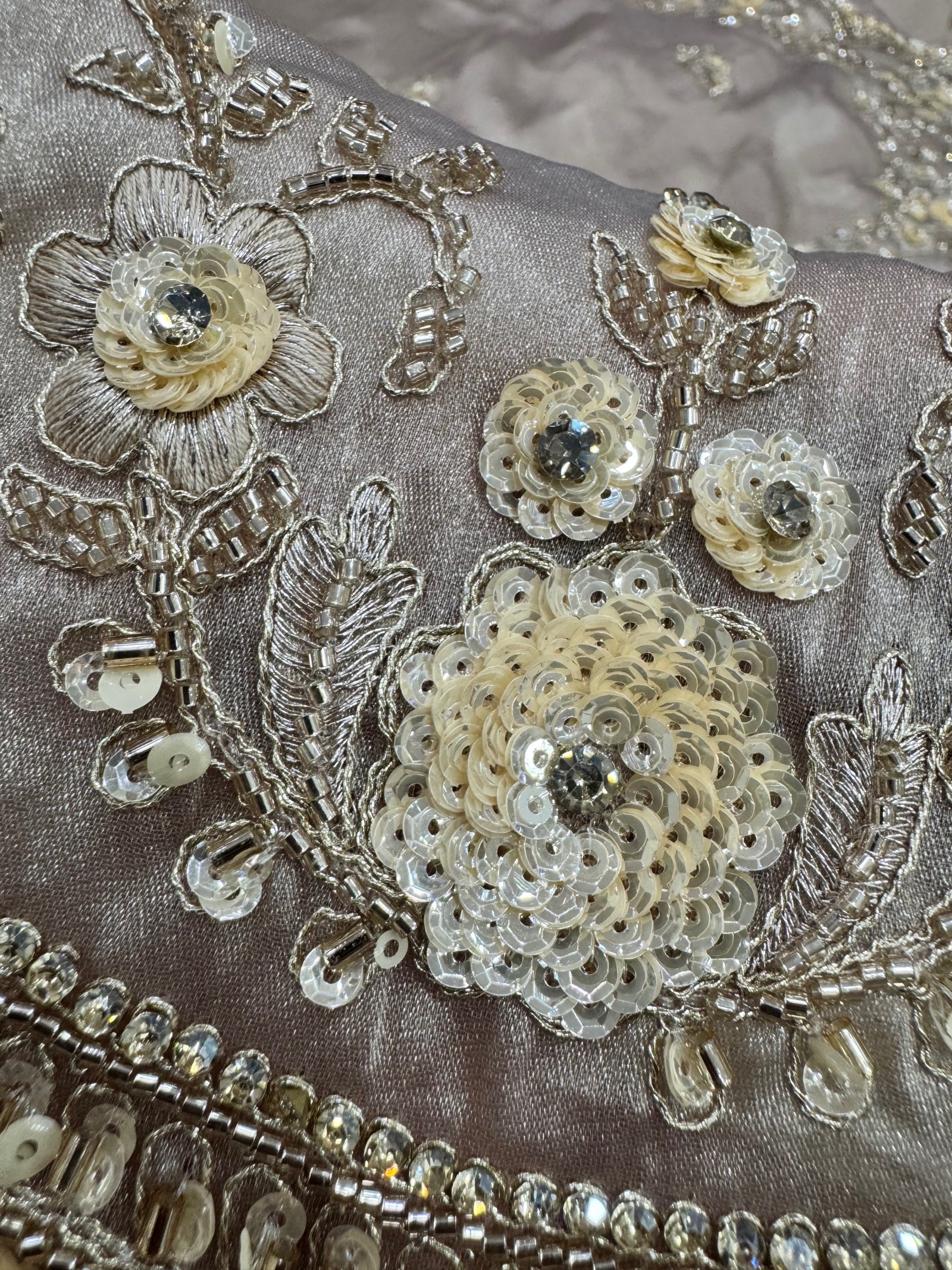Close-up of embroidered fabric with floral patterns and sequins on a beige background