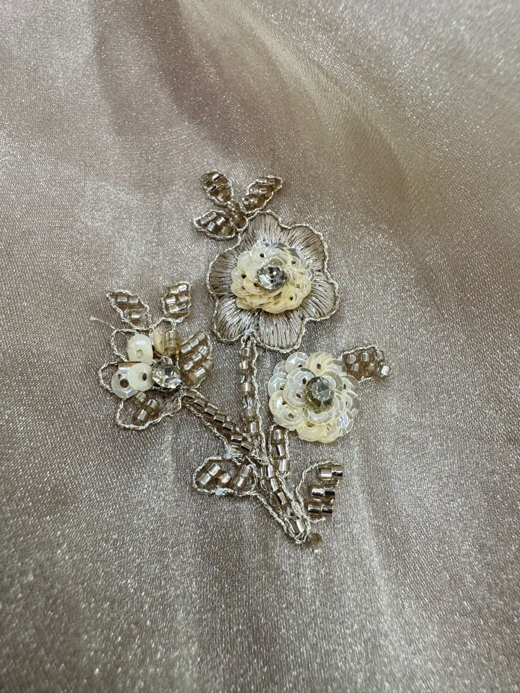 Decorative floral brooch with gold and pearl-like stones on a beige fabric background