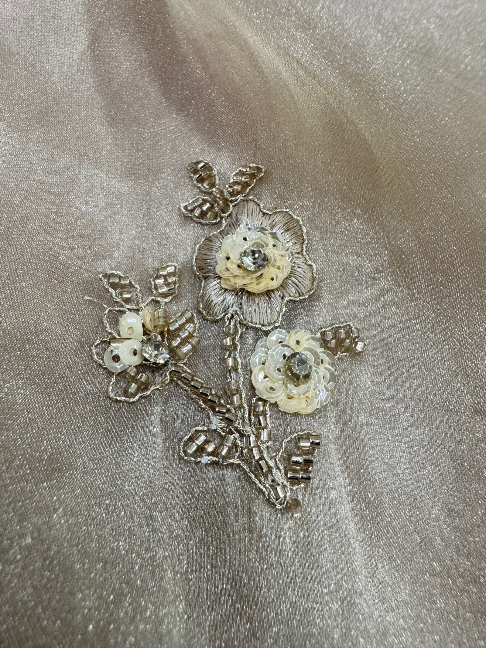 Decorative floral brooch with gold and pearl-like stones on a beige fabric background