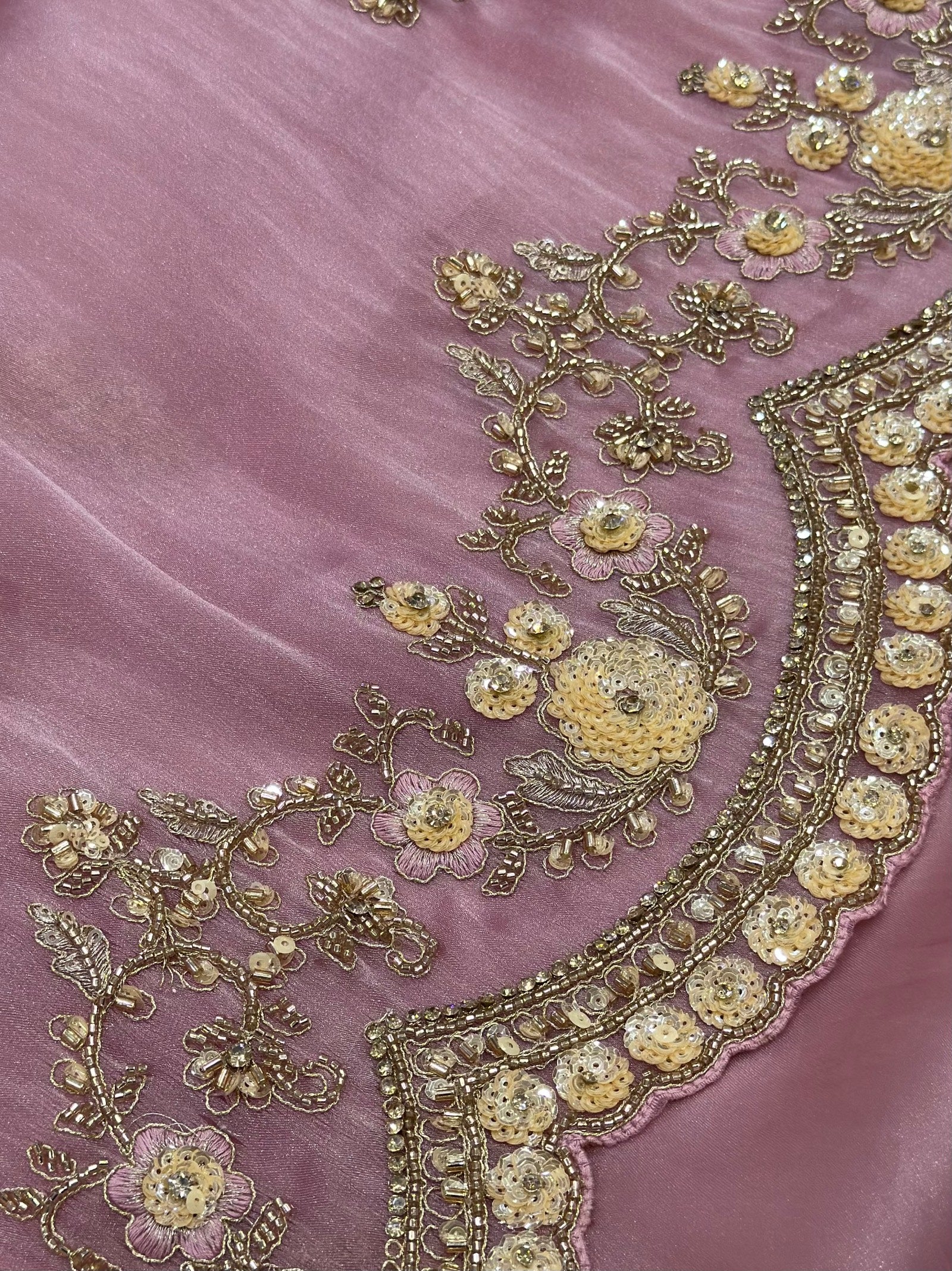 Close-up of embroidered fabric with gold details on a pink background