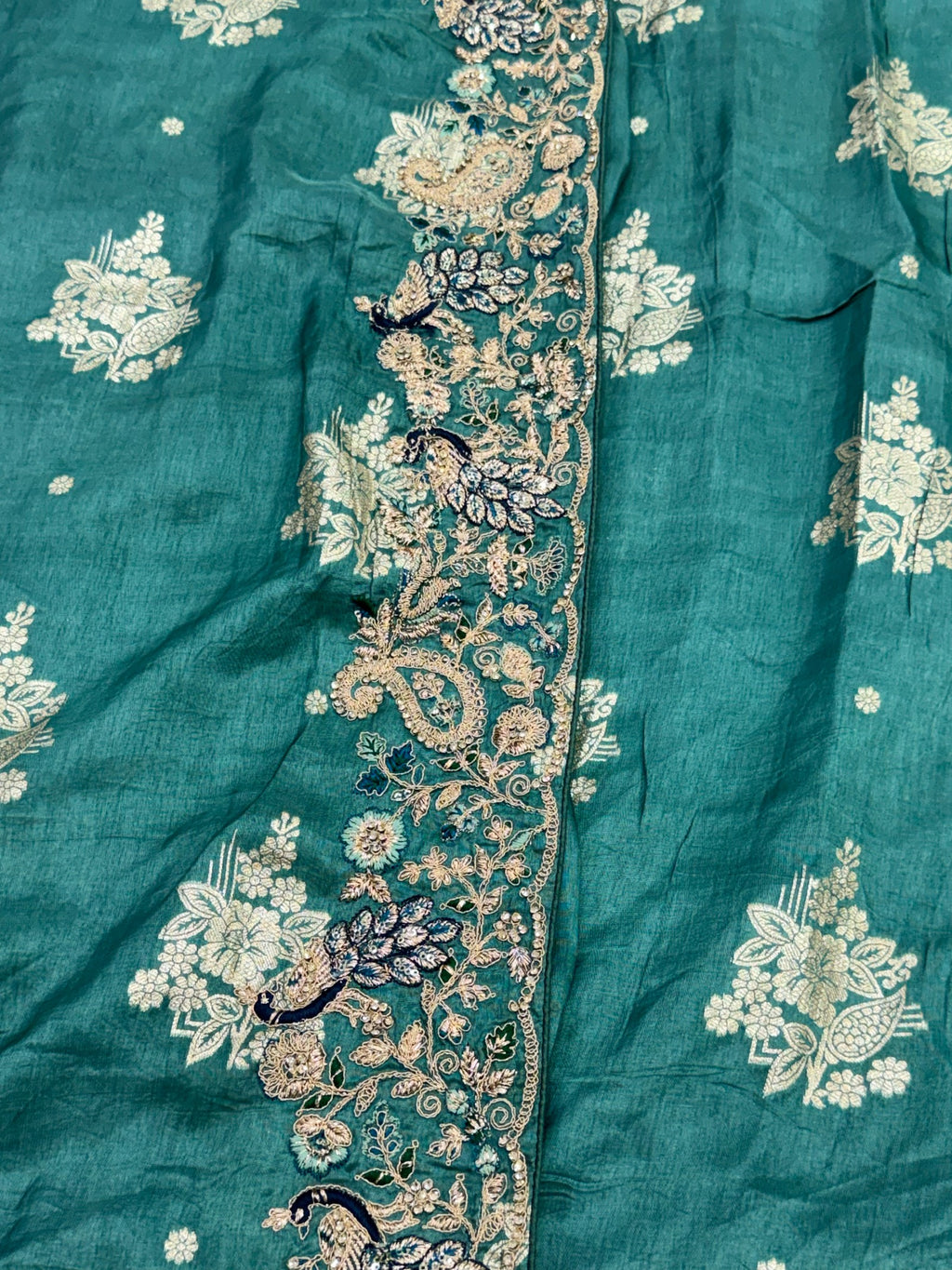 Teal fabric with intricate gold and white floral embroidery