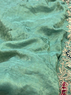Close-up of teal fabric with intricate gold and red embroidery on the edge