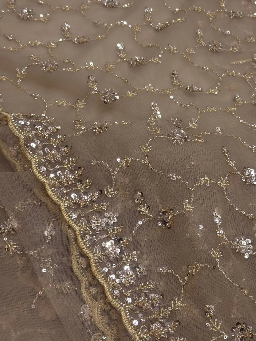 Close-up of a fabric with gold sequin and bead embellishments on a beige background