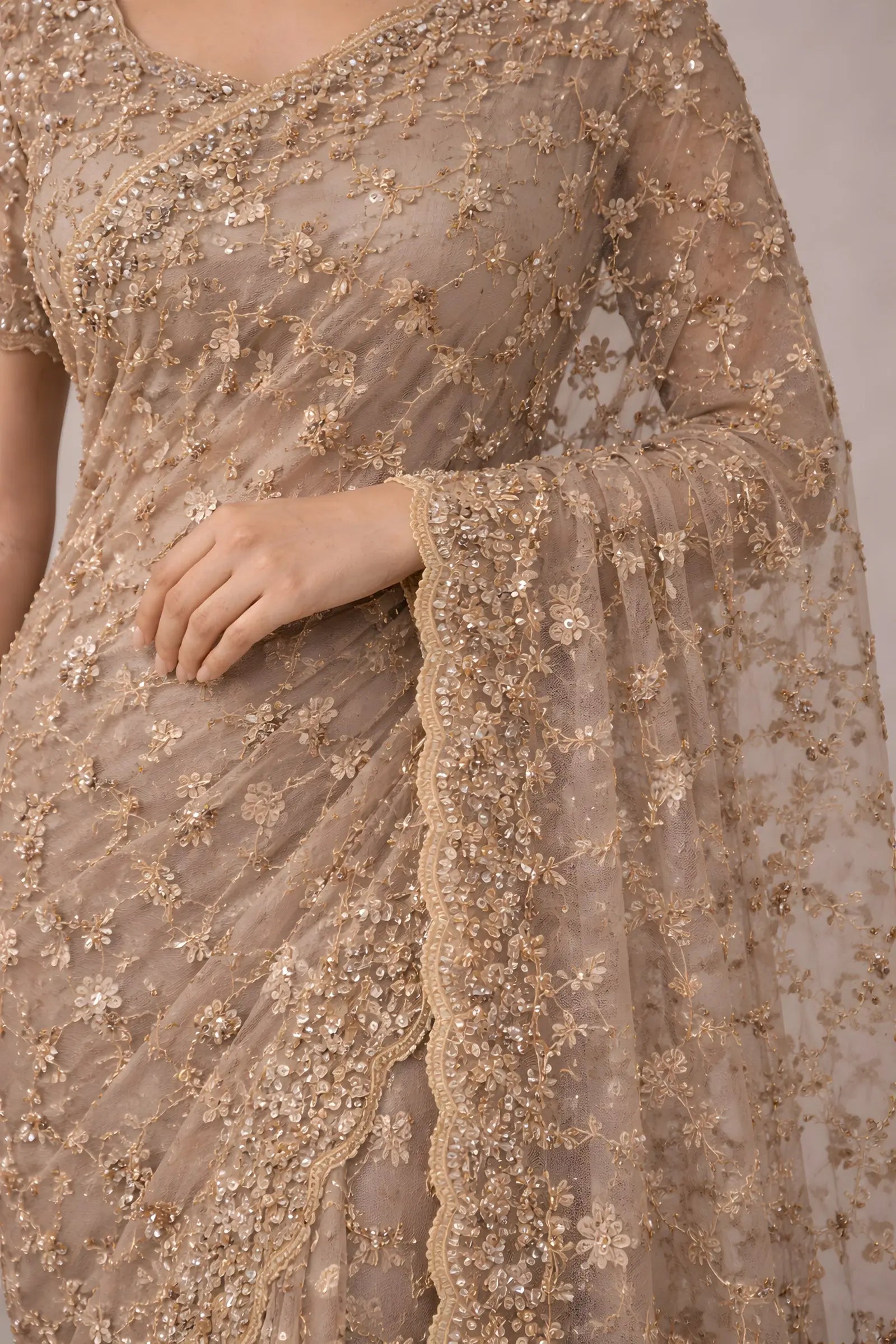 Close-up of a beige embroidered saree with a plain background