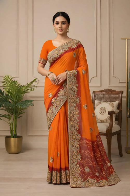 Woman wearing an orange saree with intricate patterns in a room with a plant and chair.