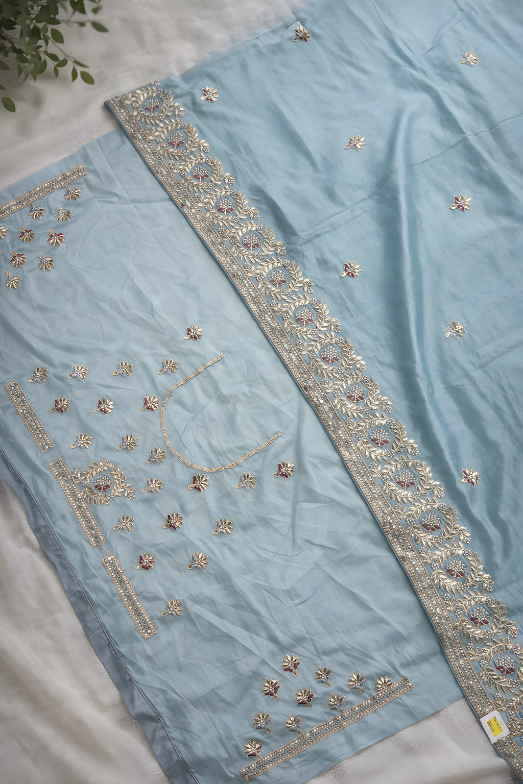 Light blue fabric with intricate gold embroidery on a white surface.