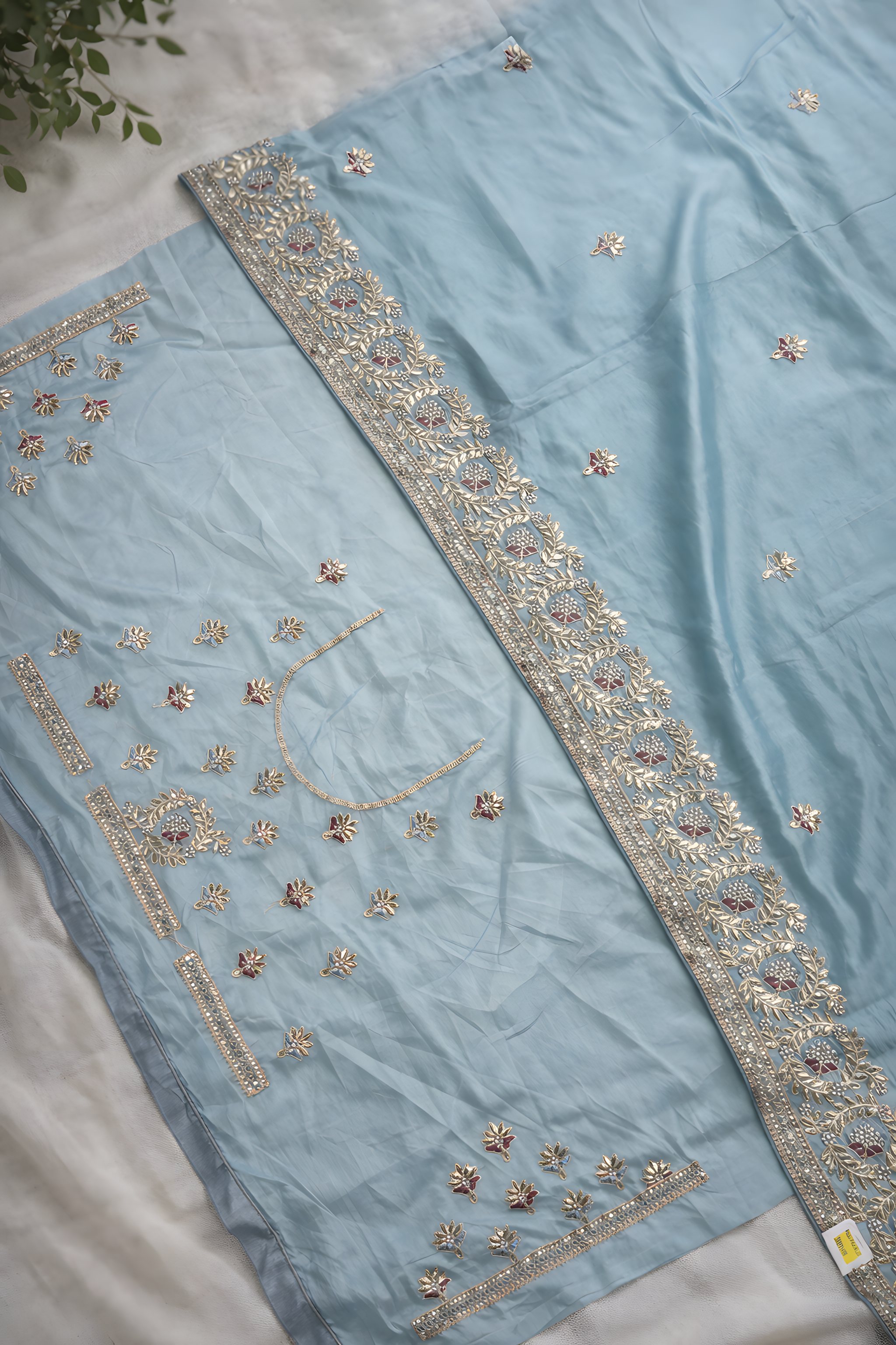Light blue fabric with intricate gold embroidery on a white surface.