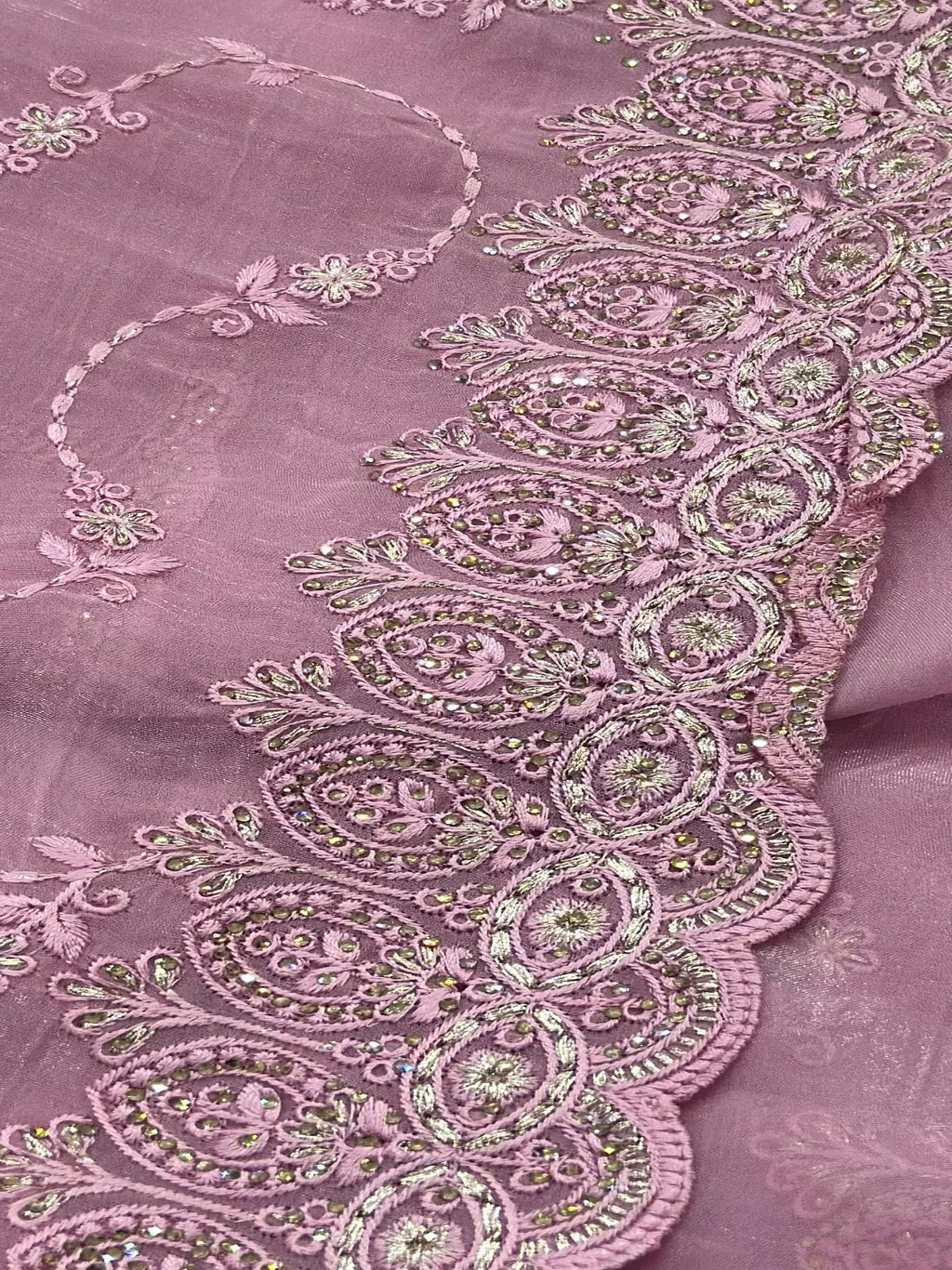 Close-up of a pink fabric with intricate embroidery and embellishments.
