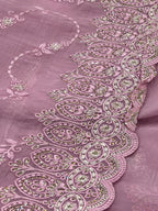 Close-up of a pink fabric with intricate embroidery and embellishments.