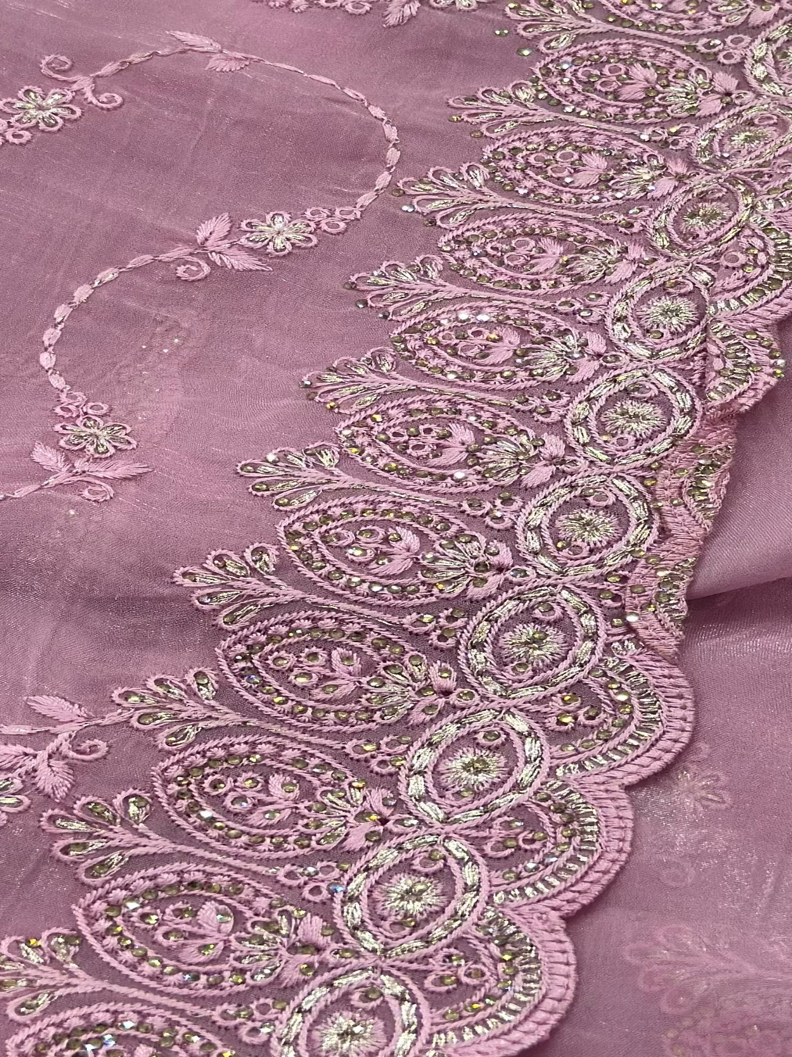 Close-up of a pink fabric with intricate embroidery and embellishments.