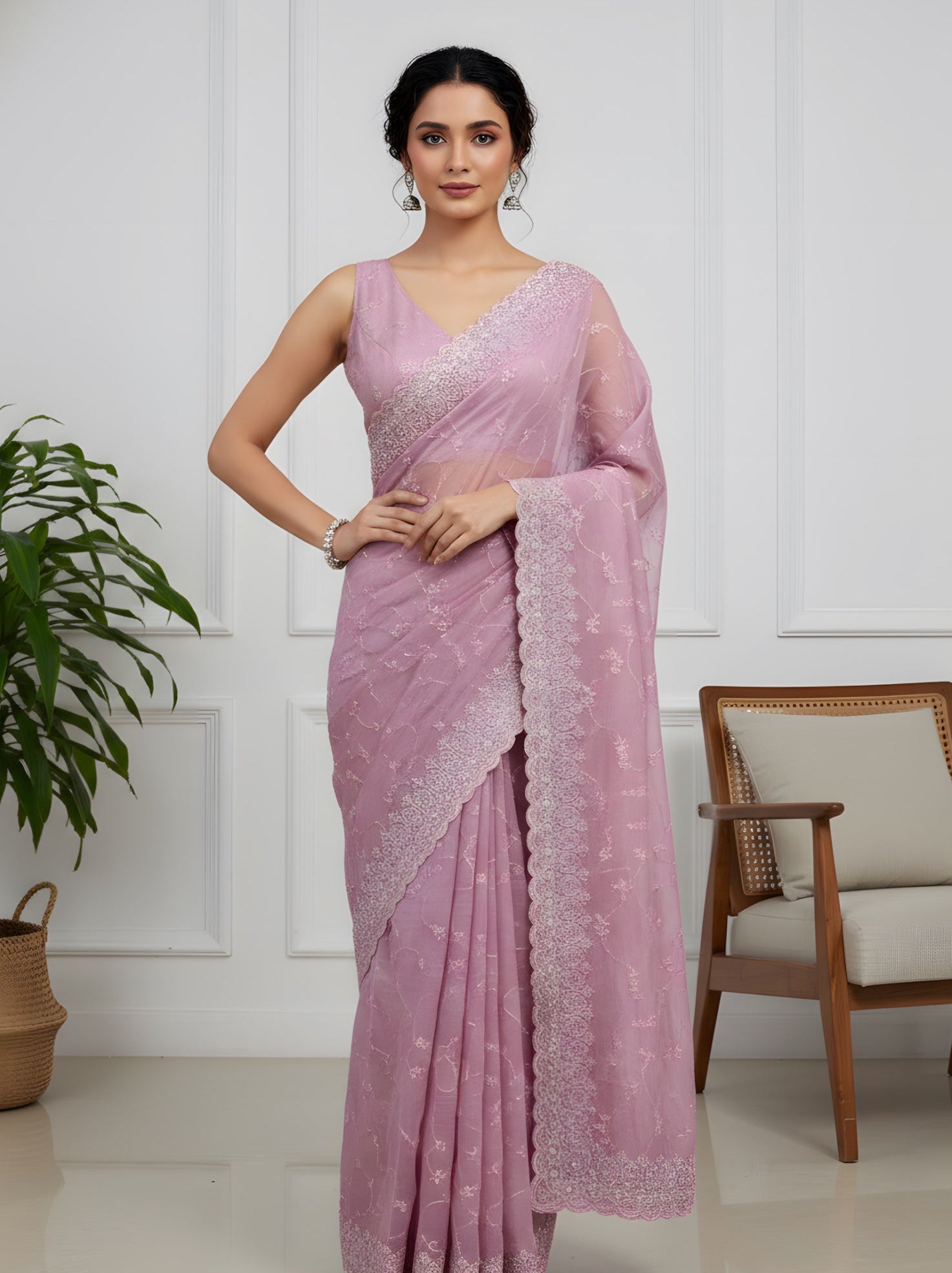 Woman wearing a pink saree in a room with a plant and chair.