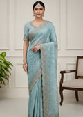 Woman wearing a light blue saree with silver patterns in a minimalistic setting.