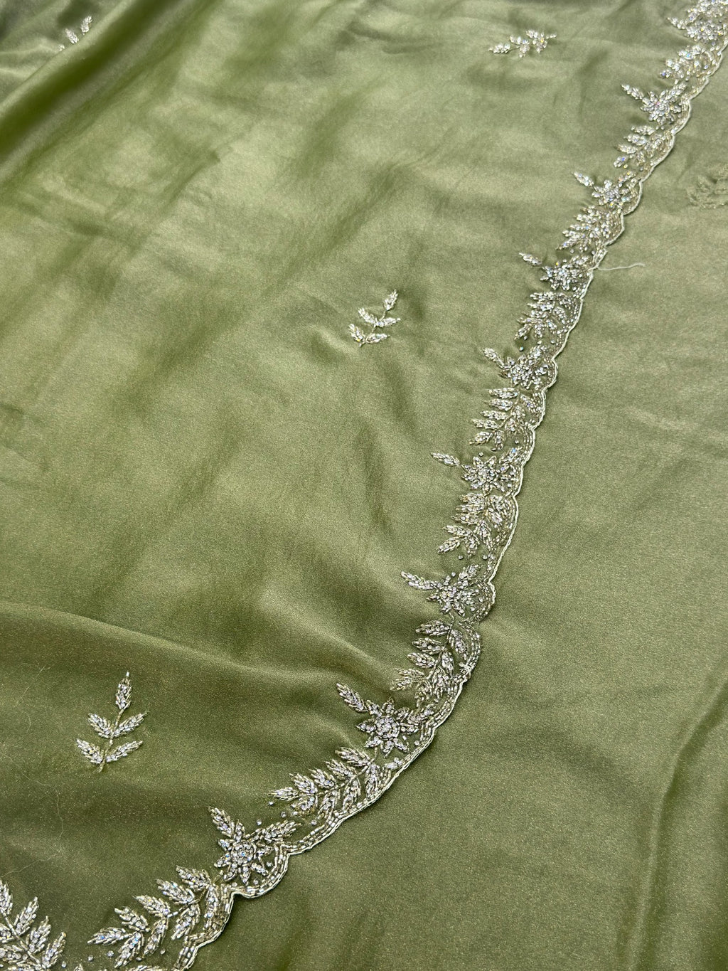 Green fabric with intricate white embroidery along the edge