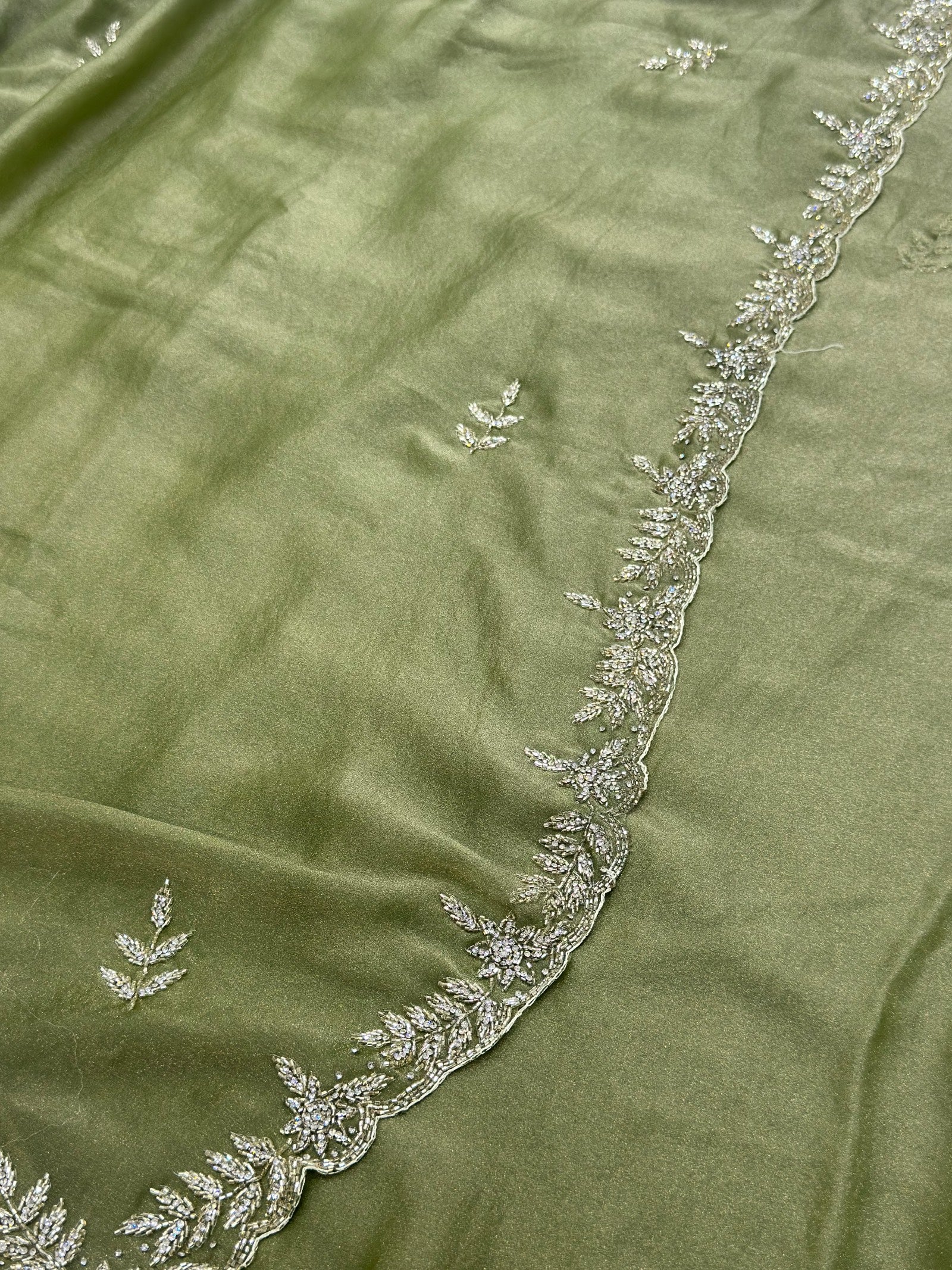 Green fabric with intricate white embroidery along the edge